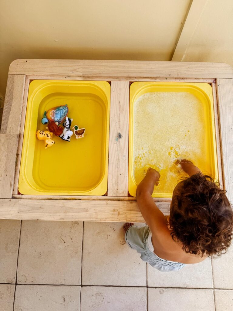 Little boy playing with trays of water, learning how to 'wash' his toys in soapy water.