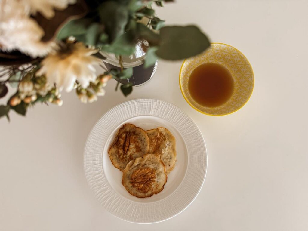 Eggless pancakes with a side of maple syrup and a vase of flowers in the corner.