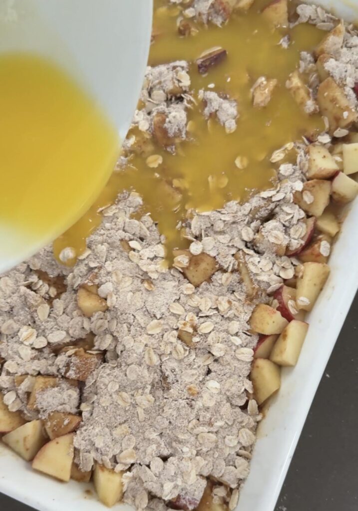 Pouring butter over apple crumble before baking