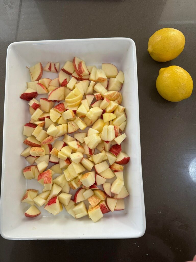 Chopped apples in ceramic dish with lemons on the side, ready to make a healthy nut-free apple crumble.