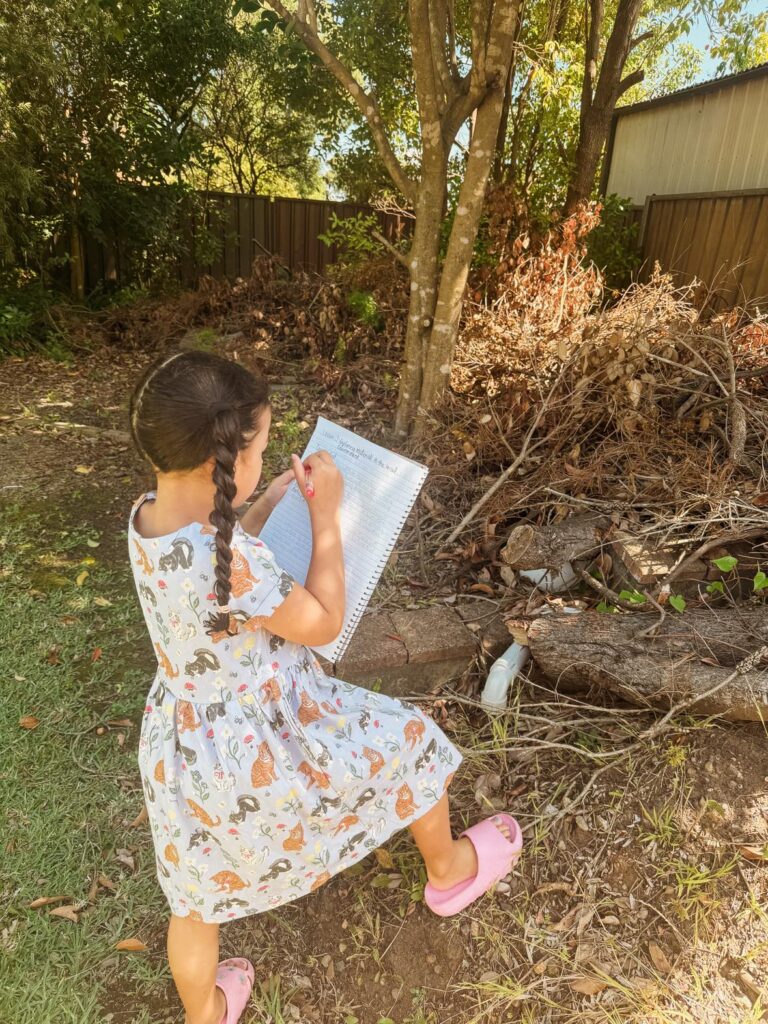 Girl taking notes outside while observing her backyard. 