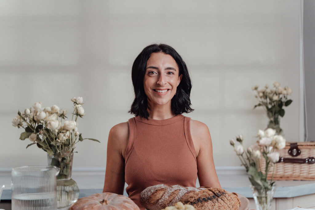 Jess at The Wholesome Mama smiling in front of a sample of delicious food and next to some white flowers.