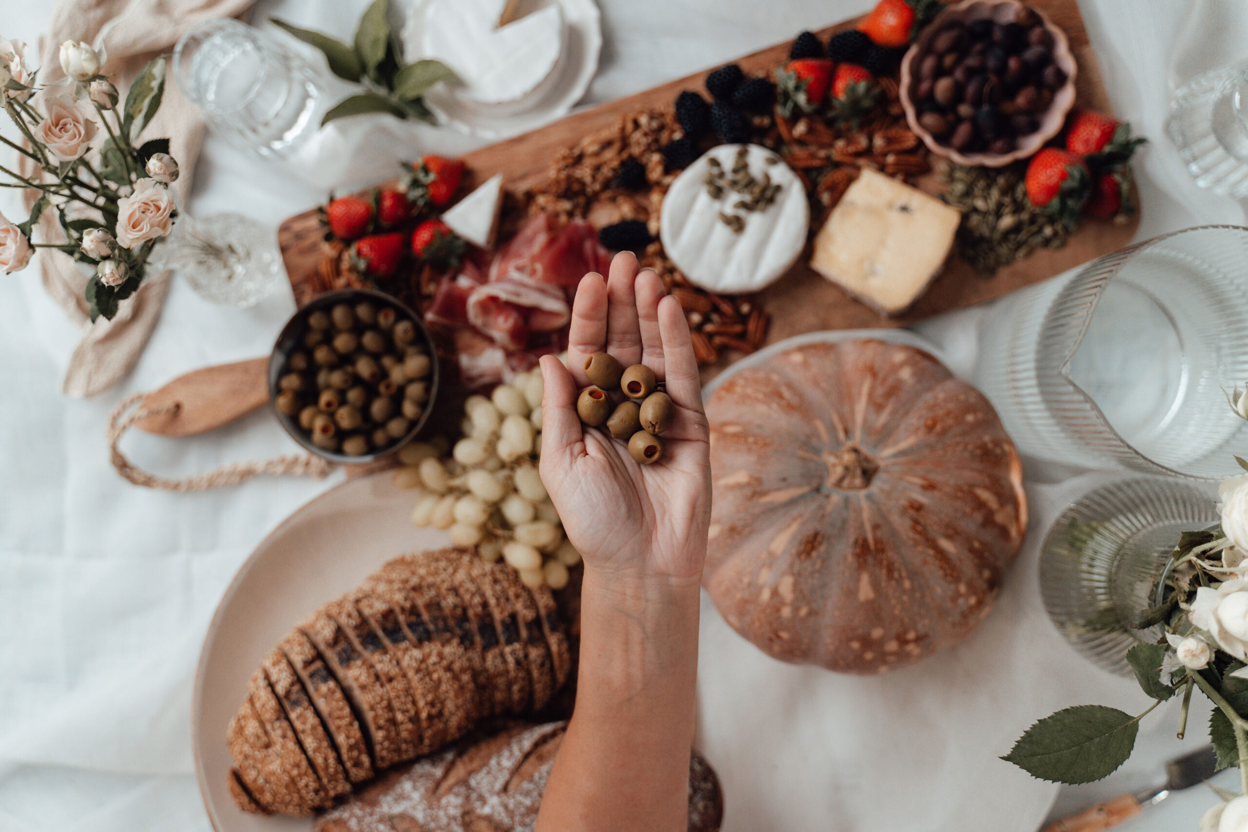 Woman holding handful olives over table of food.