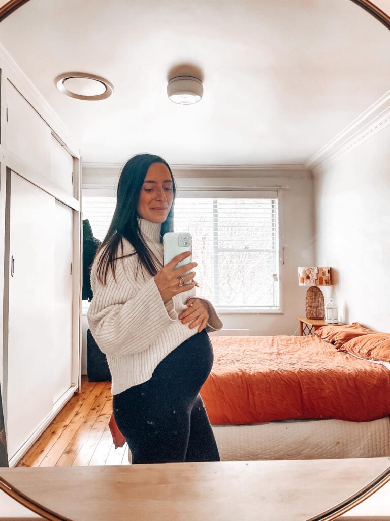 Woman taking selfie of pregnant belly at 20 weeks pregnant.