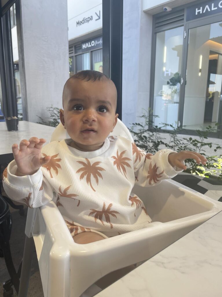 My 10 month old son sitting in a high chair at a restaurant waiting for something to eat.