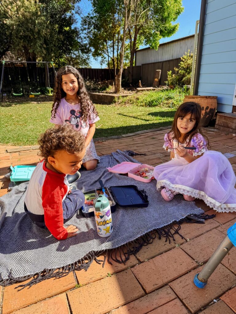 7 FAQ About our Homeschool Life in Australia: Three kids having a picnic in the backyard