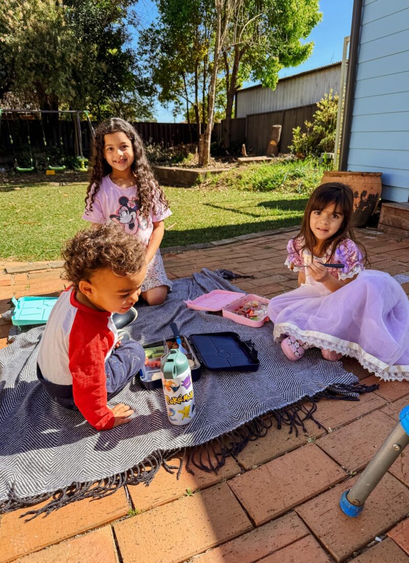 Our Homeschool Life in Australia FAQ: Three kids having a picnic in the backyard