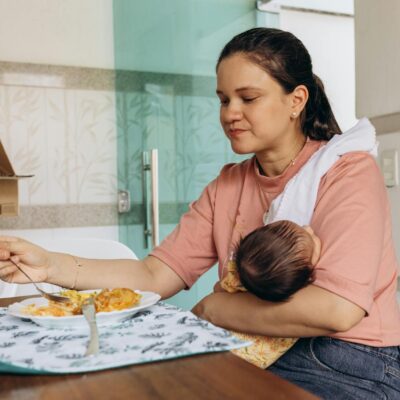 A mother eating at the table while holding her baby, depicting a warm family moment.