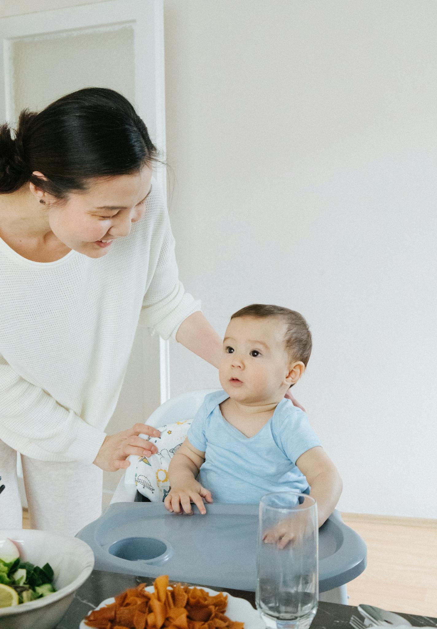 A mother lovingly engages with her baby during a meal at home, creating a warm family moment.