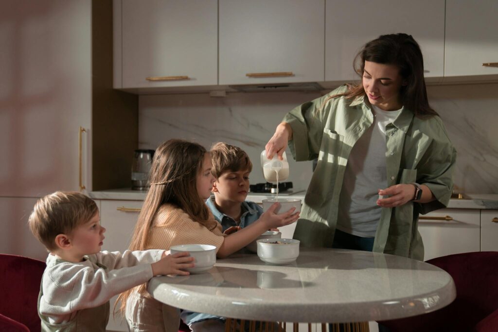 A mother pours milk into bowls for her three children during breakfast time at home.